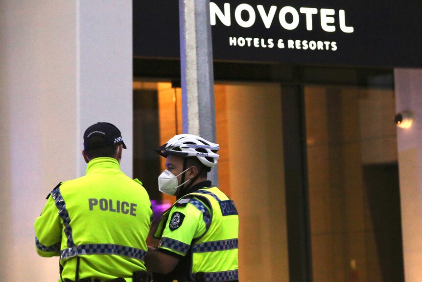 Two police officers wearing face masks stand outside the Novotel hotel on Murray Street in Perth WA.