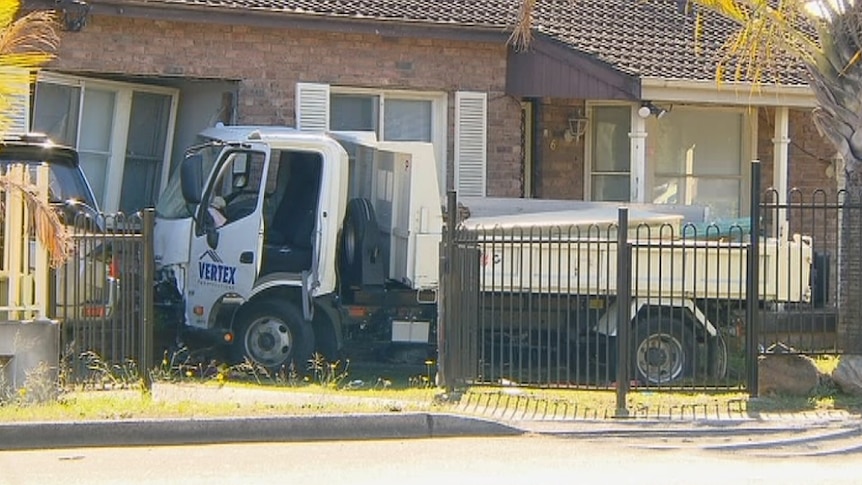 A white truck with its front bumper touching the front of a brick house.