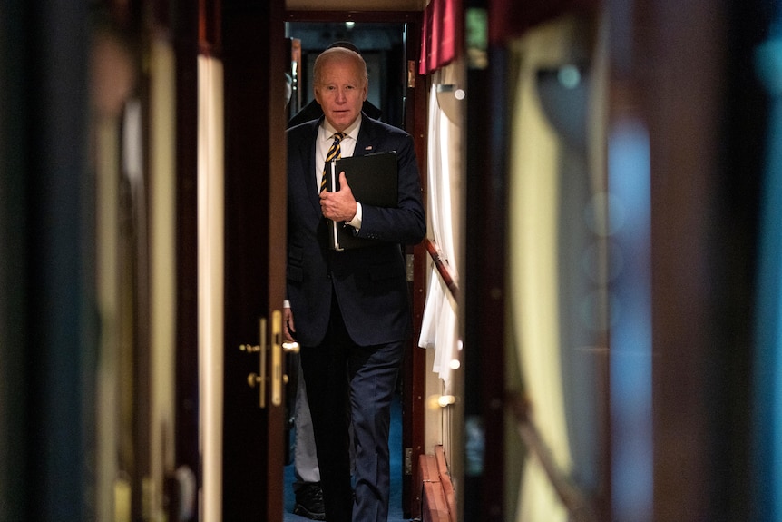 Mr Biden walks down a narrow train cabin. 
