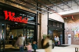 One entrance to the Westfield Marion store, with red neon sign, red bricks and people rushing in