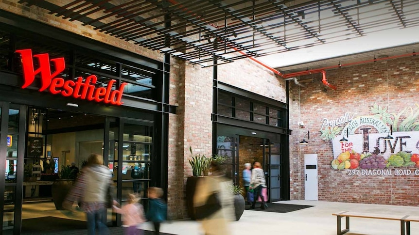 One entrance to the Westfield Marion store, with red neon sign, red bricks and people rushing in