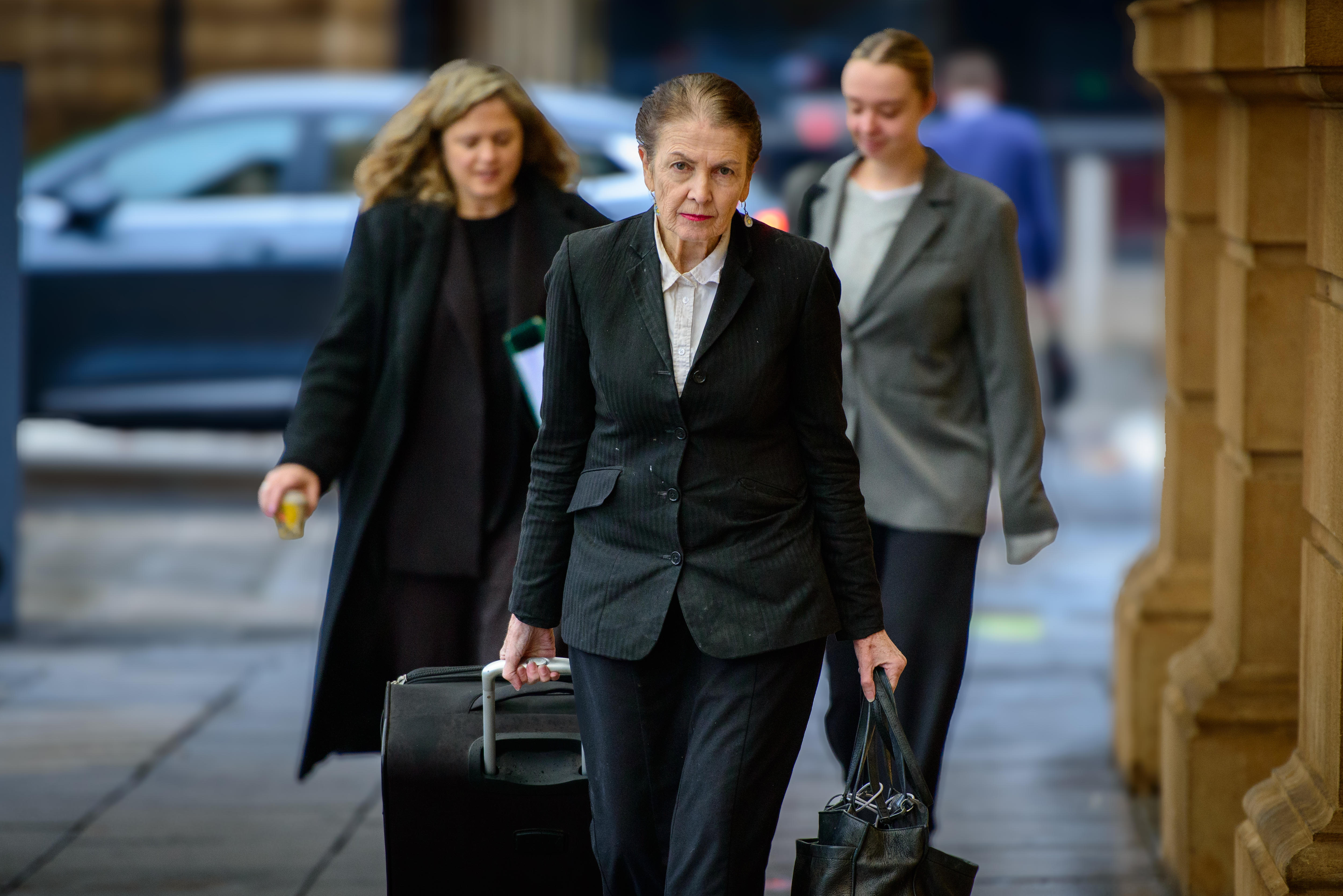 A woman in a black suit is walking along a footpath carrying bags.