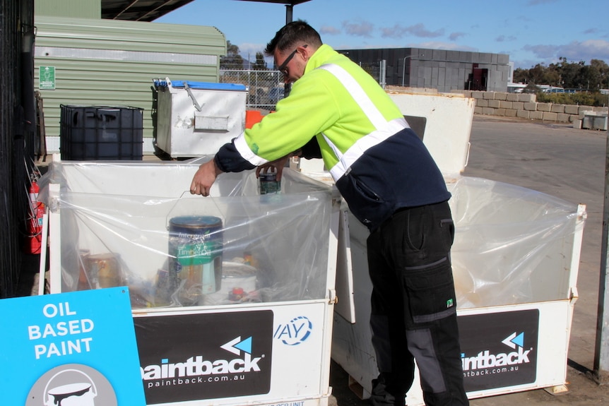 Waste management worker sorts paint tins into recycling collection drop off bins.