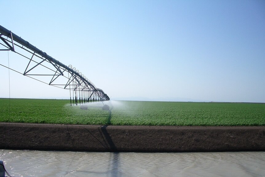 A large centre pivot irrigation system with an irrigation channel in the foreground.