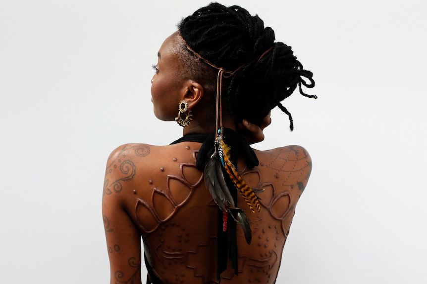 A model displays her tattoos and body modifications, showing her back and side of her face.