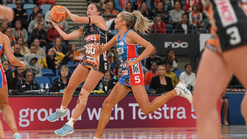 A netballer catches the ball mid-air as a defender races to keep up with her.