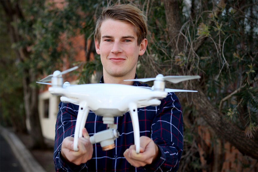 Jake Lapham holds a white drone in front of his face.