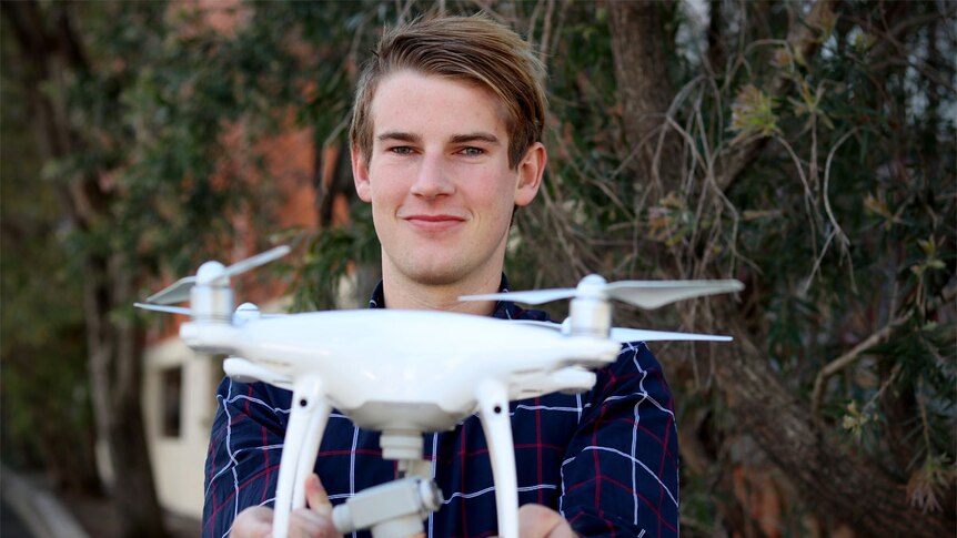 Jake Lapham holds a white drone in front of his face.