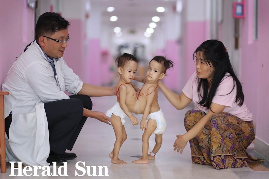 A doctor crouches in a hospital corridor in Bhutan with Dawa and Nima and their mother Bhumchu Zangmo.