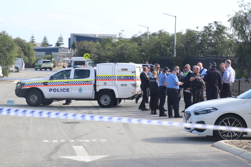 A large contingent of police in a car park next to a police vehicle. 