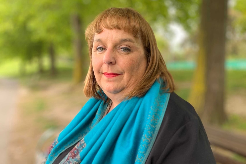 A woman wearing a bright blue scarf is sitting on a park bench on a sunny day.