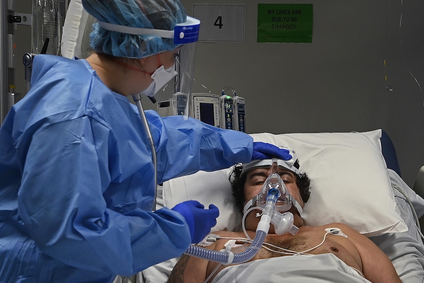 A staff member touches a man's head while he lies in bed.