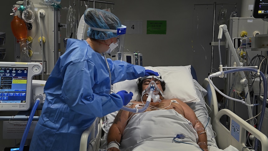 A staff member tuoches a man's head while he lies in bed.