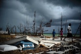 Residents on the island of Grand Bahama walk over the ruins of a building, with a shattered coffin in the front of the image.