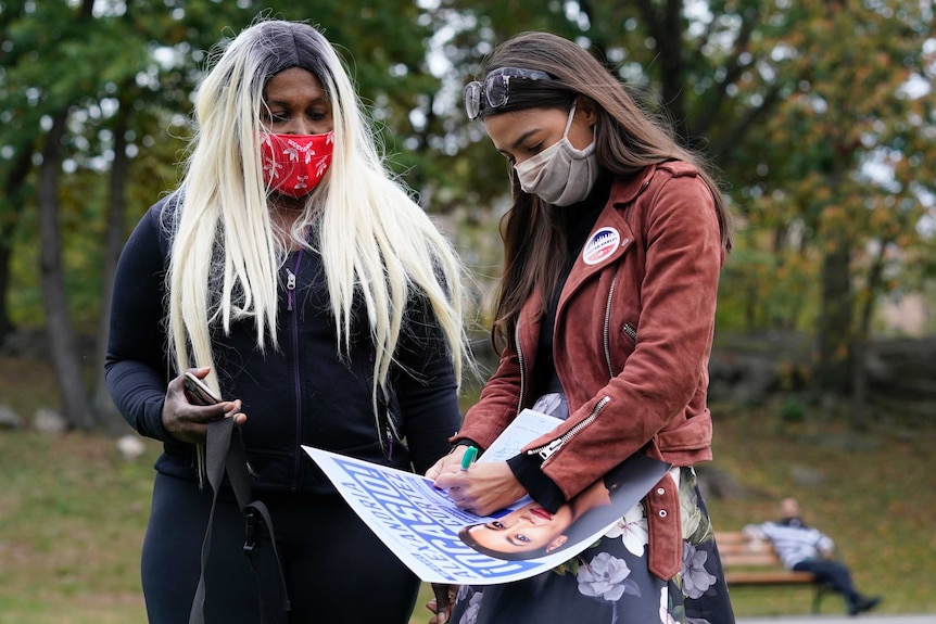 Two women stand outside with one signing a poster