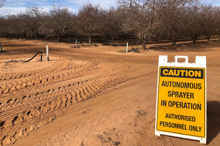 A yellow sign warns people that autonomous almond sprayers are operating in the area 