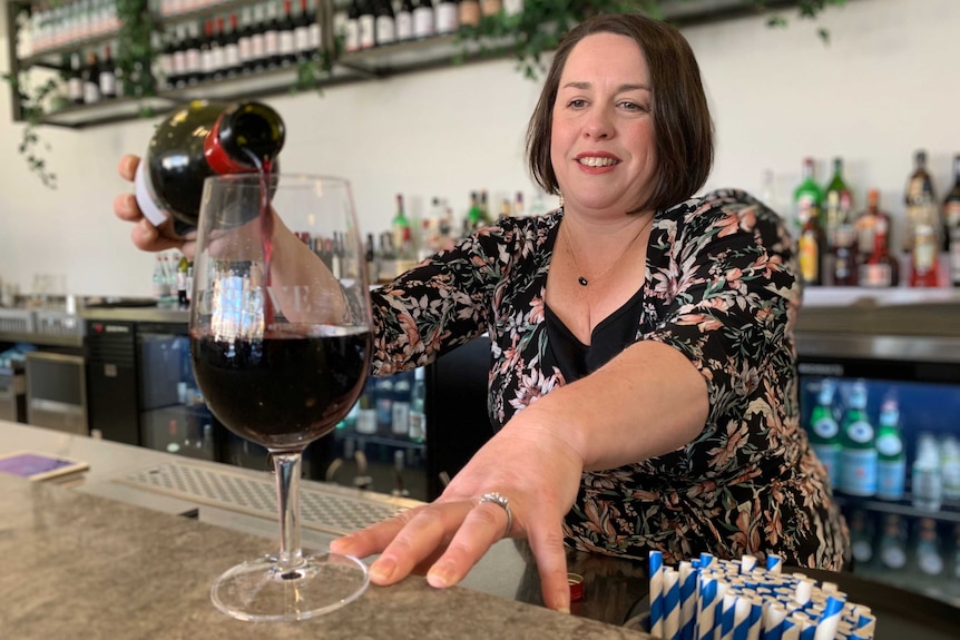 Emily Blades stands behind the bar and pours a glass of red wine.