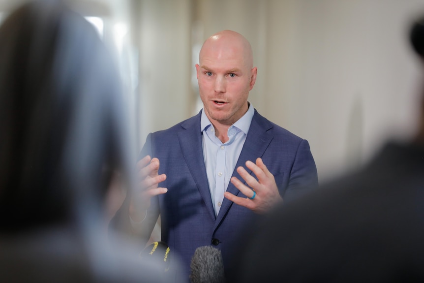 a man in a suit talking at a press conference 