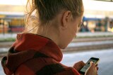 A close up looking over the shoulder of a woman using her mobile phone on the platform of the train station.