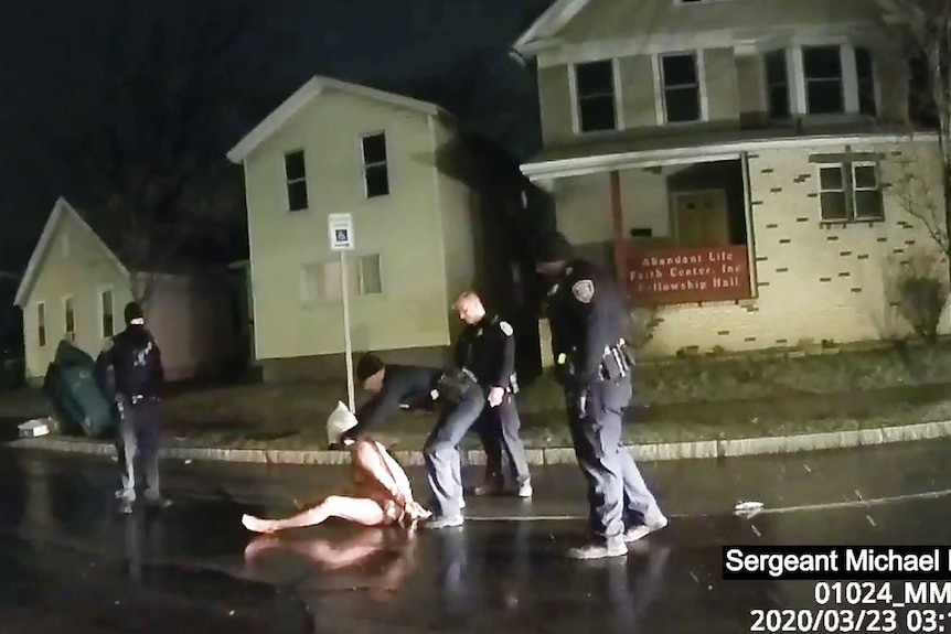 A Rochester police officer puts a hood over the head of Daniel Prude as he sits on the ground naked.