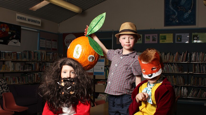 Children dressed as Roald Dahl characters sit on a desk in the library.