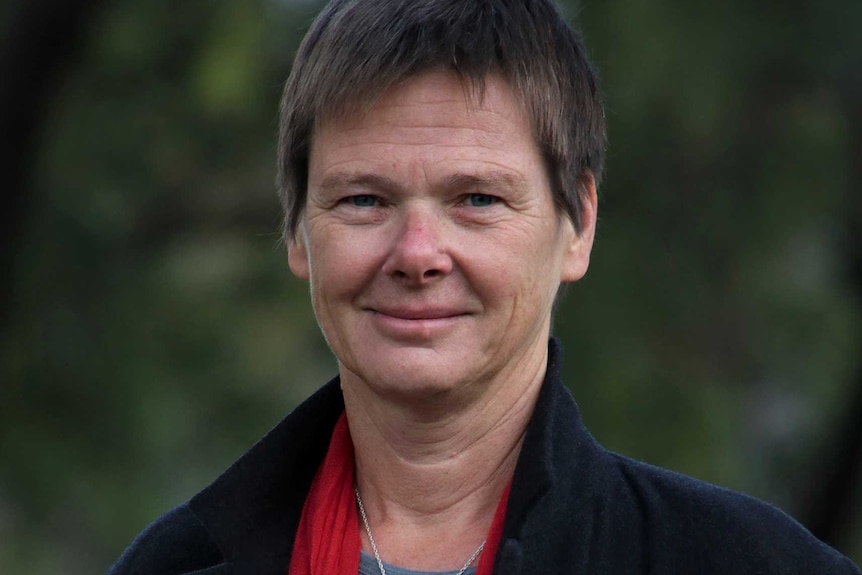 A woman in a black jacket and red scarf stands in a park.