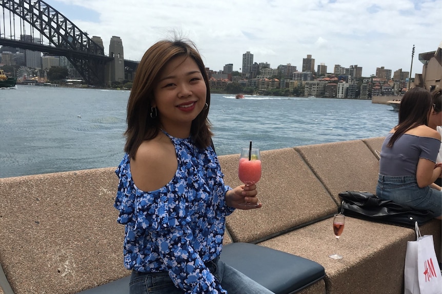 一个华人女性坐在海边，手中拿着饮料