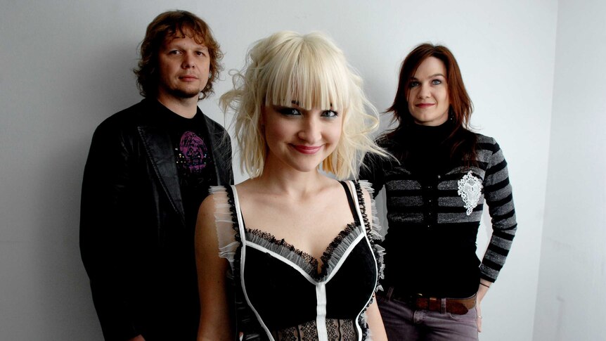 A band photo consisting of three people: A man with shaggy hair, a woman with brown hair and a woman with blonde hair and fringe