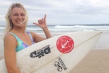Brooke Mason gives a 'rock-on' hand signal while holding her surfboard at the beac at Snapper Rocks on the southern Gold Coast.