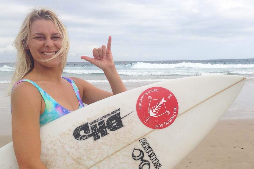 Brooke Mason gives a 'rock-on' hand signal while holding her surfboard at the beach at Snapper Rocks on the southern Gold Coast.