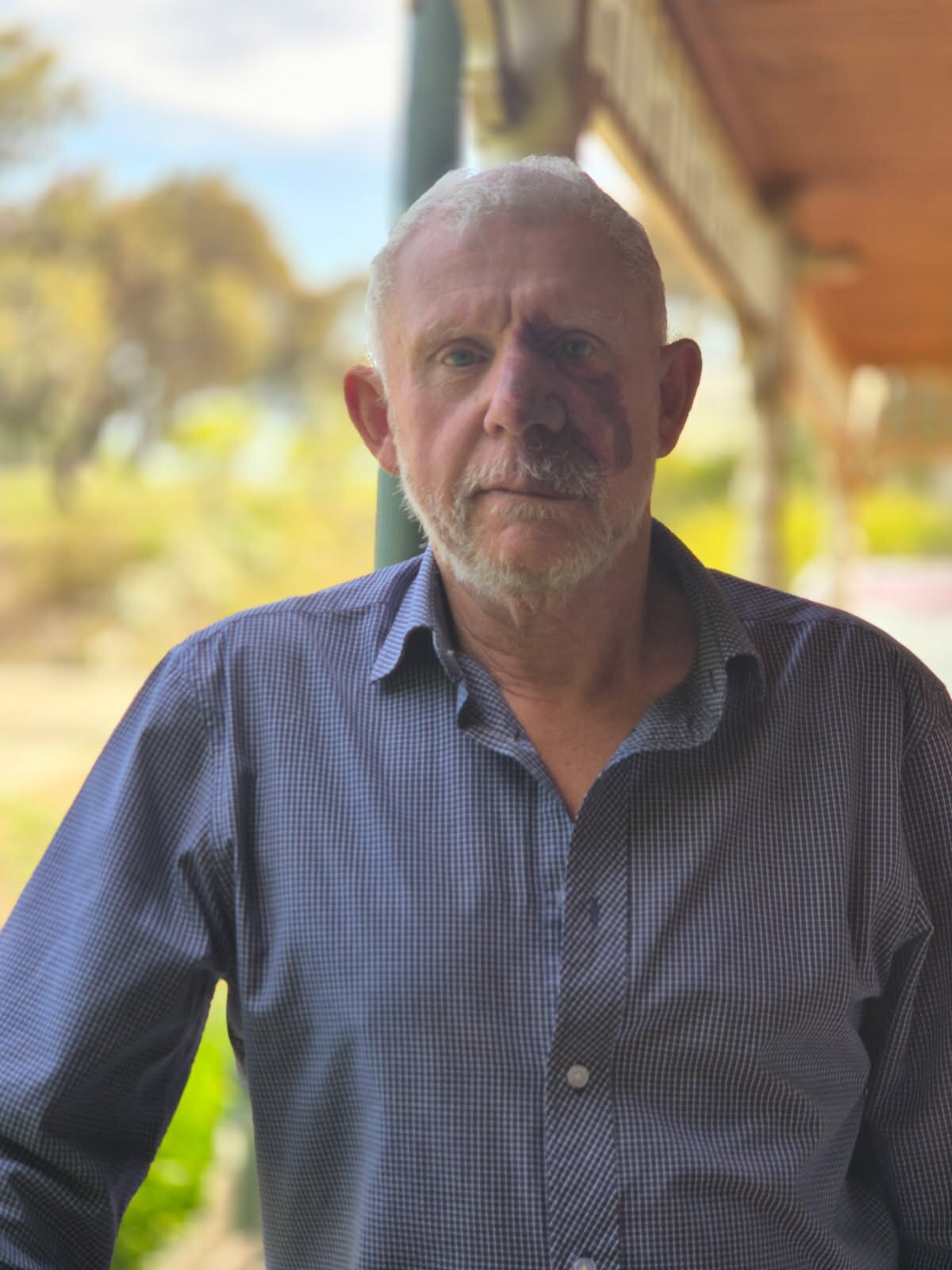 homem com cabelos grisalhos e barba curta, olhando para a câmera com fundo desfocado.