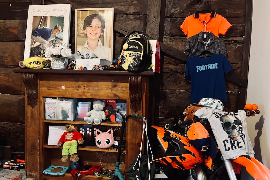 a wooen shelf holding photos of Will, stuffed animals, orange hi-vis shirt, a minicycle arranged as a memorial to him