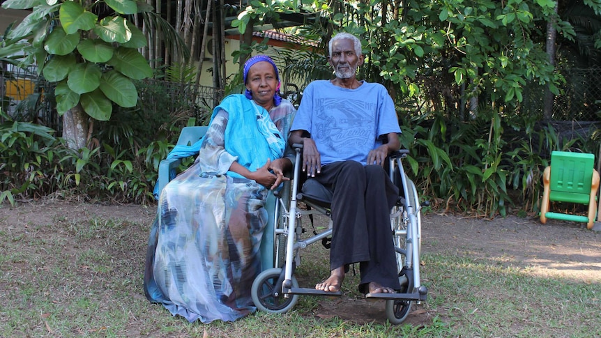 A woman in traditional Somali dress sits next to her husband in a leafy green Darwin backyard.