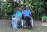 A woman in traditional Somali dress sits next to her husband in a leafy green Darwin backyard.