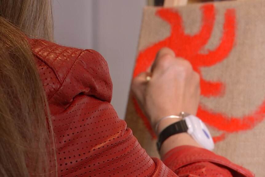 A woman painting something orange on a canvas.