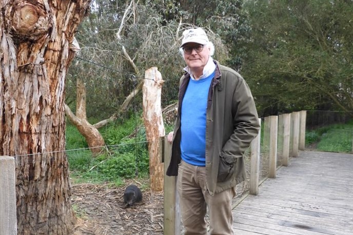 A man stands next to an enclosure with a Tasmanian Devil inside