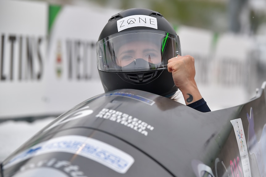 Bree Walker clenches her fist from inside her bobsled, wearing a helmet