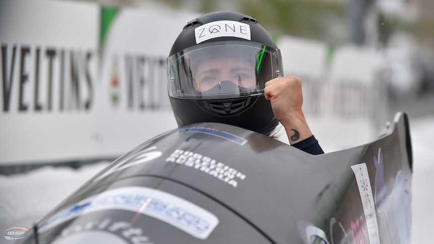 Bree Walker clenches her fist from inside her bobsled, wearing a helmet