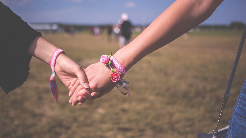 Two women holding hands at a music festival.