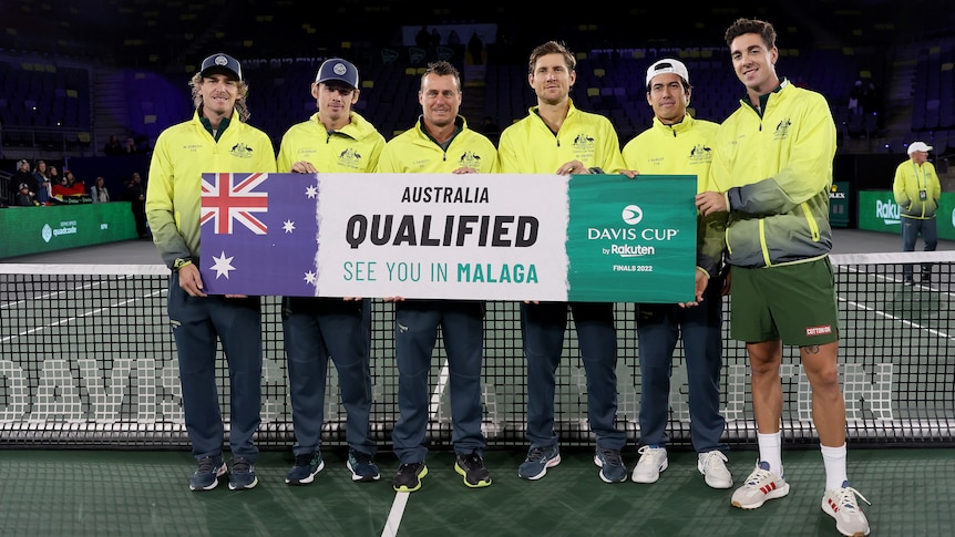 A group of five Australians wearing gold jackets stand on court holding a sign saying 'Australia qualified see you in Malaga'.