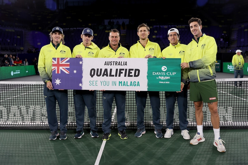 A group of five Australians wearing gold jackets stand on court holding a sign saying 'Australia qualified see you in Malaga'.