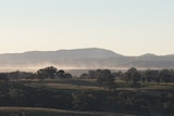 Sunset view of dust rising above paddocks and distant mine site