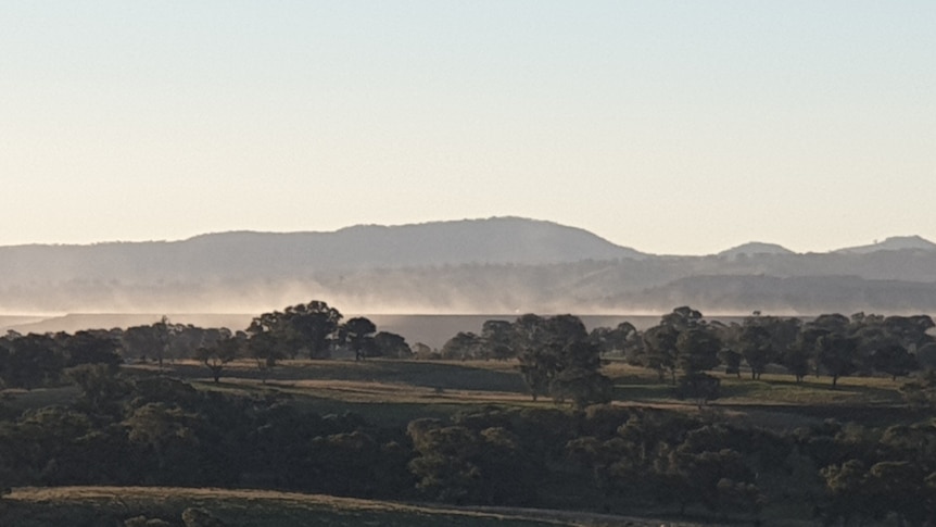 Sunset view of dust rising above paddocks and distant mine site