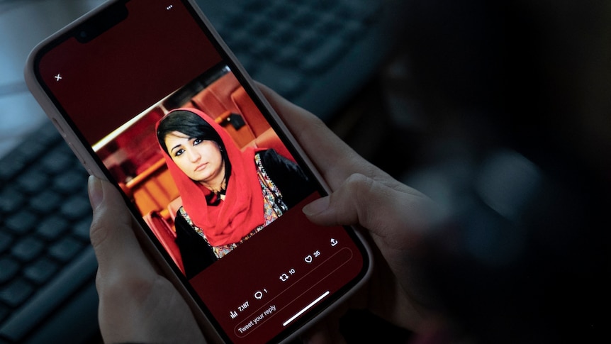 A woman looks at a picture of former Afghan lawmaker Mursal Nabizada on her mobile phone. She is wearing a red headscarf