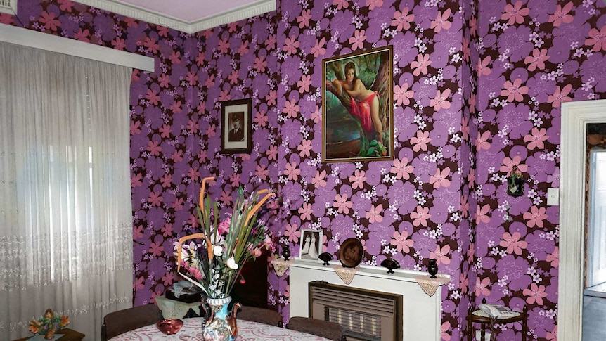 You view a dining room with bold purple and pink wallpaper with a flower motif framing 1970s-era furniture.