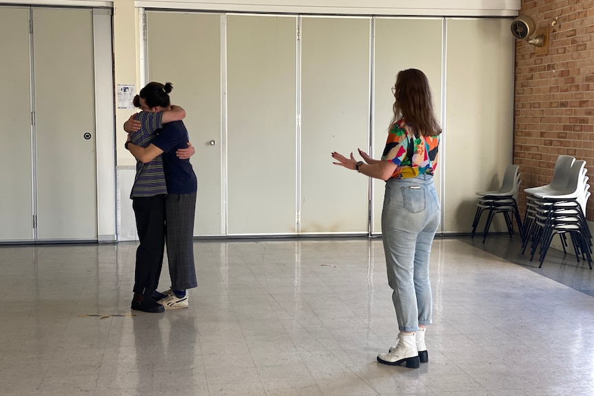 A woman faces two actors who are cuddling.