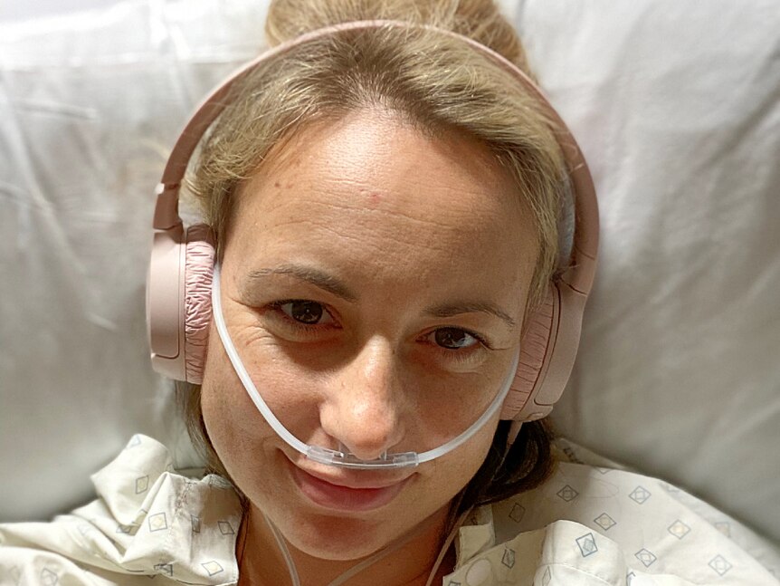 Woman laying in hospital with headphones on and tubing through nose. Gently smiling.