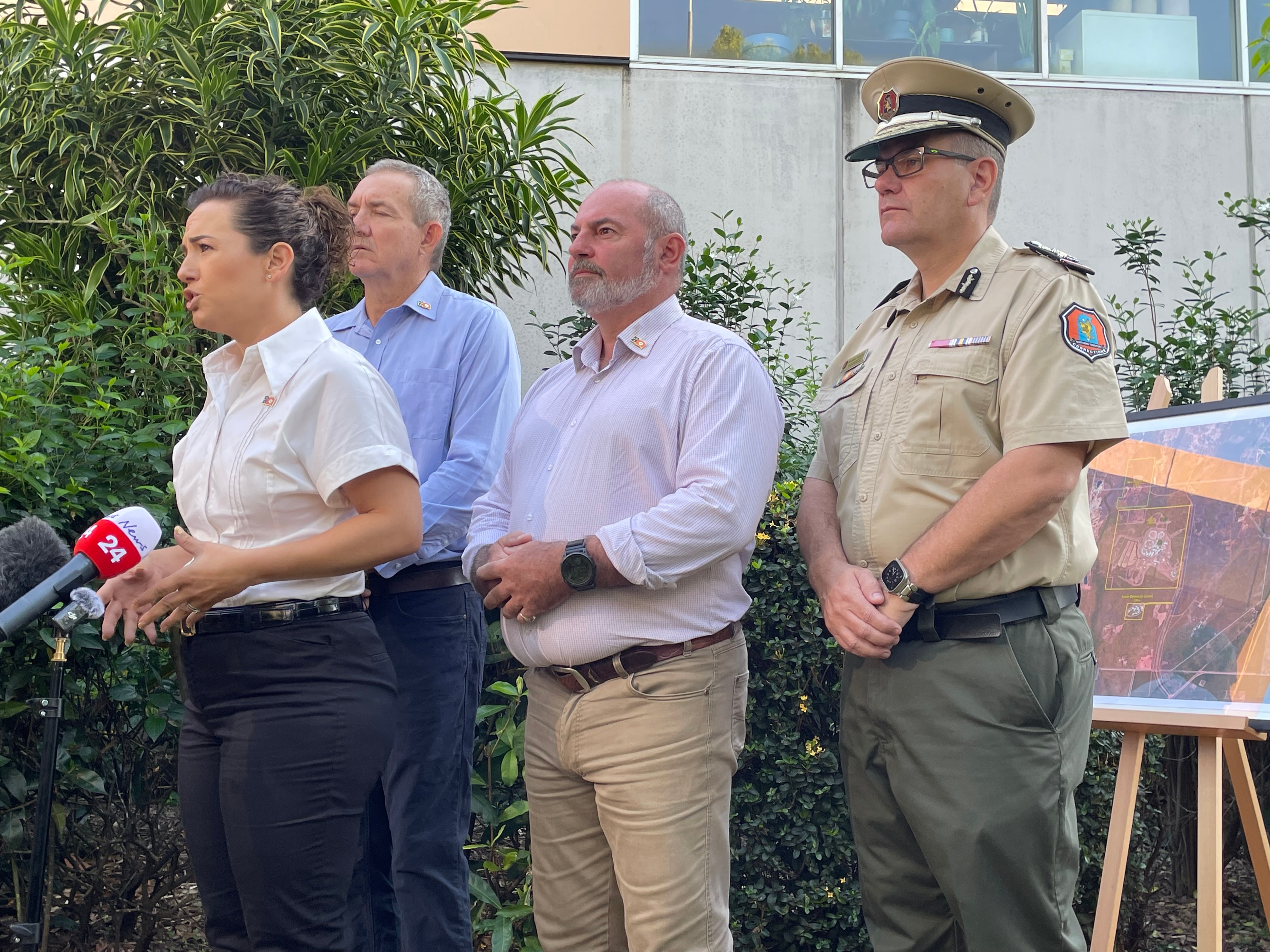 Lia Finocchiaro stands behind a microphone with three men behind her, one in a police uniform