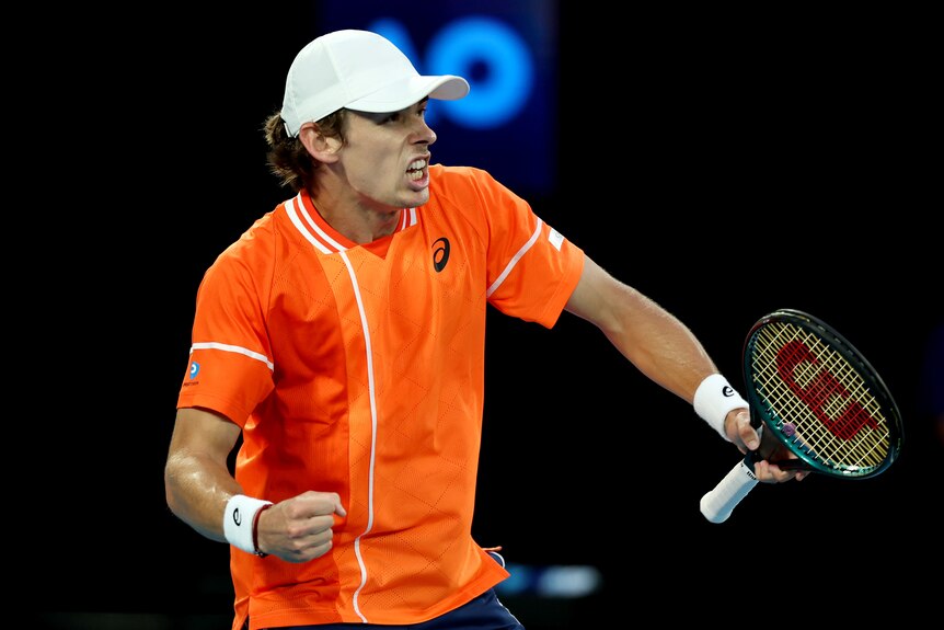 A male tennis player in an orange shirt, roars and pumps his fist in celebration.