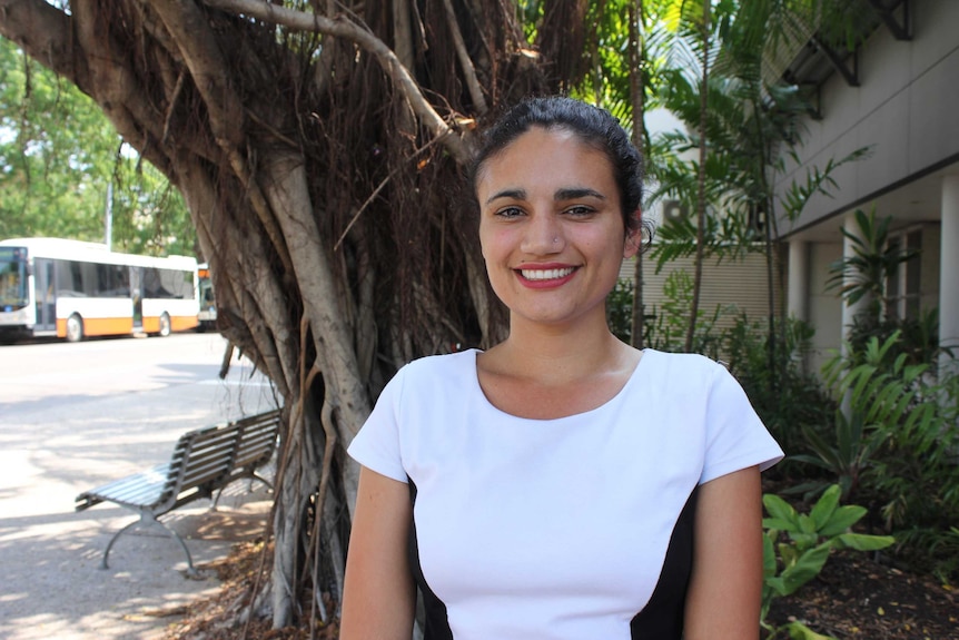 A woman with red lipstick stands in front of a tree in Darwin.